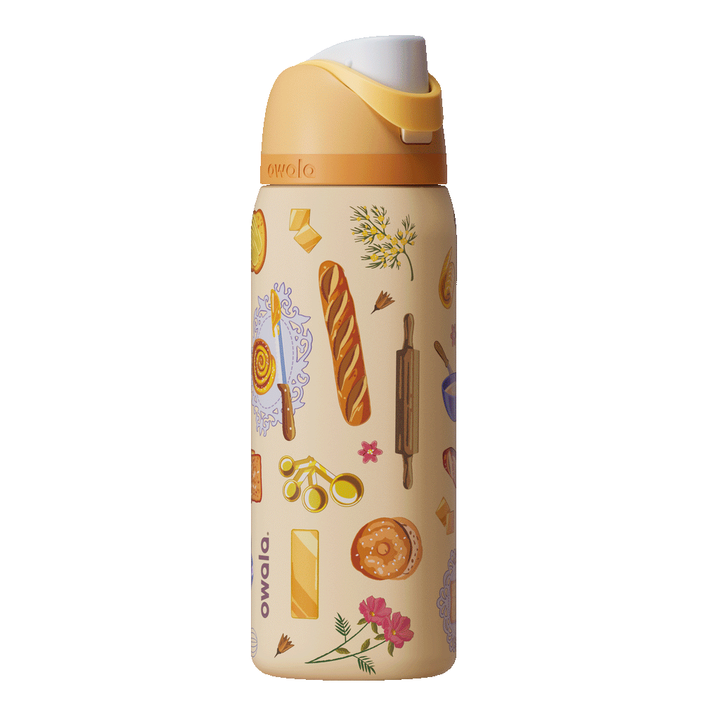FreeSip 32oz Brunch Bunch; rotating view of warm cream body covered in illustrated brunch food graphics including baguettes, pastries, croissants, eggs, rolling pins, and floral sprigs, with golden yellow flip cap, cream carry loop, and orange lid accent band